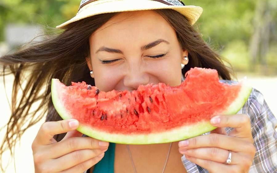 Woman similing as she eats a slice of Watermelon.