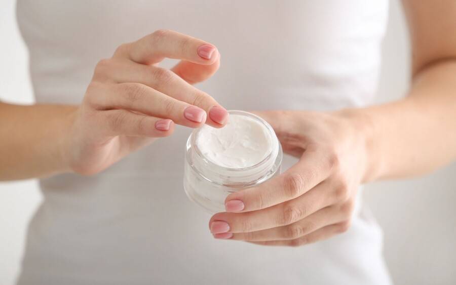 A woman opening a beef tallow moisturizer for skin care.