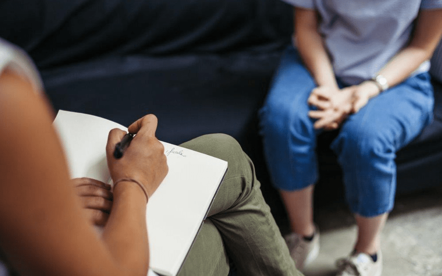 Behavioral health patient and provider talking in a sessions, while the provider is taking notes.