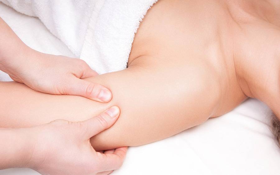 A physical therapist performs lymphedema treatment on the upper arm of a patient who is wrapped in a white towel.