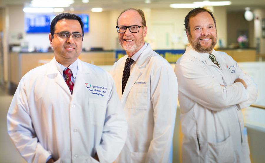 Scripps transplant physicians, Drs. Anuj Mahindra, James Mason and Jeffrey Andrey, standing and smiling in a medical facility lobby, representing the collaborative and compassionate care at Scripps for blood and marrow transplant.