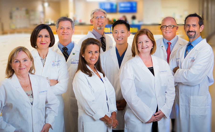 A group of Scripps transplant physicians smile whole standing in a medical facility lobby, representing coordinated care for transplantation at Scripps.