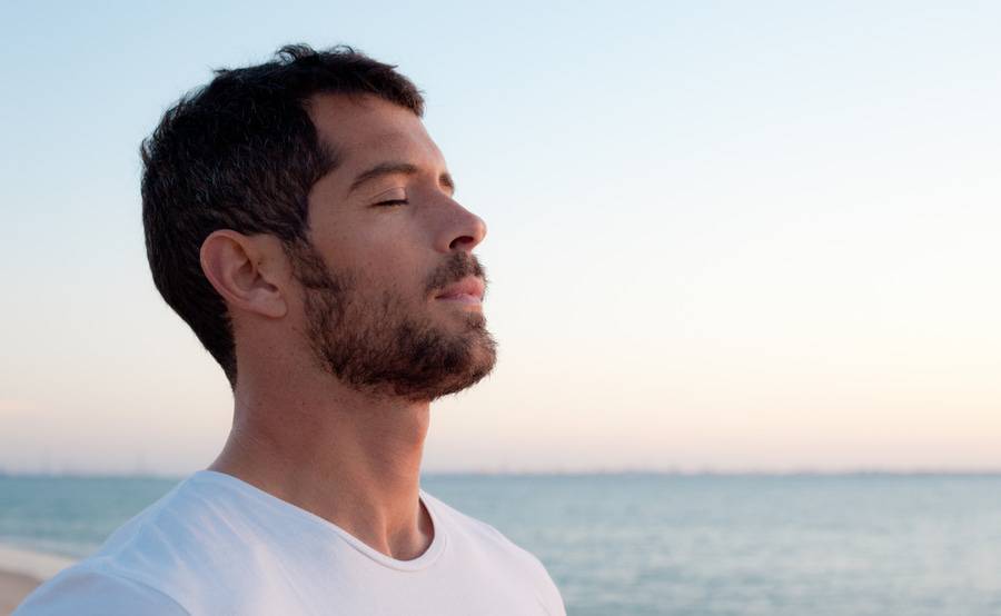 A man takes a deep breath on the beach, representing an improved quality of life with expert care for blood disorders.