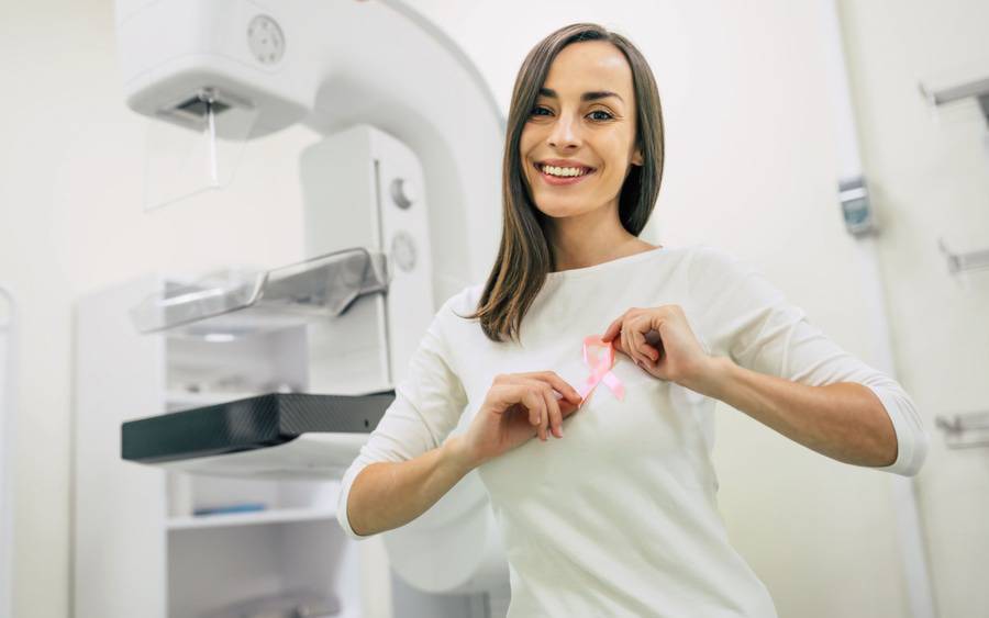 Woman with breast implants holding pink ribbon symbol before mammogram.