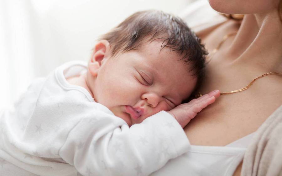 An infant rests on a mom's chest, representing breastfeeding and nursing.