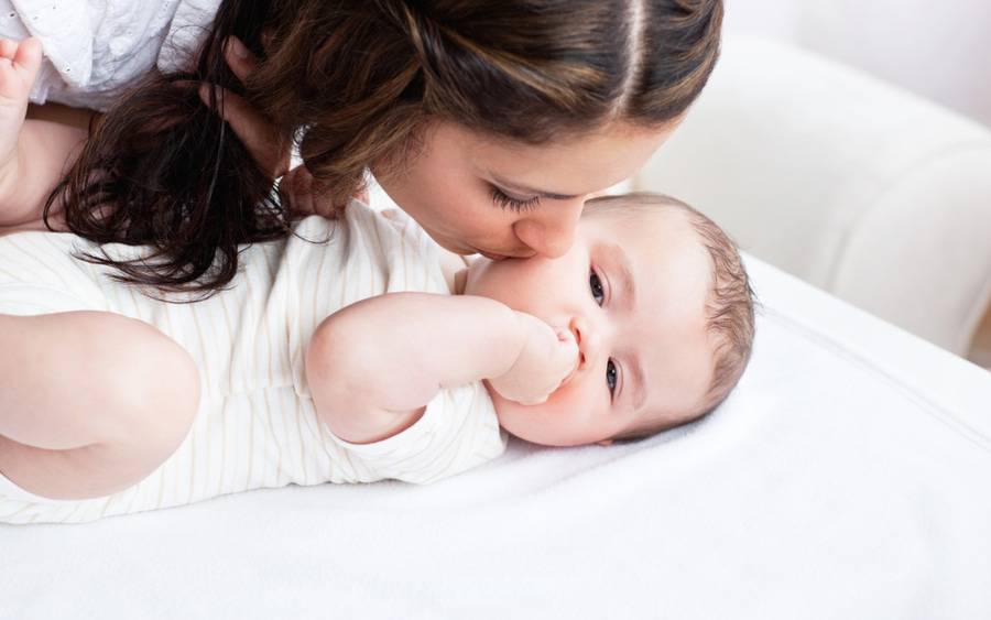 A woman gently kisses an infant on the cheek, representing the critical bonding time with a newborn.