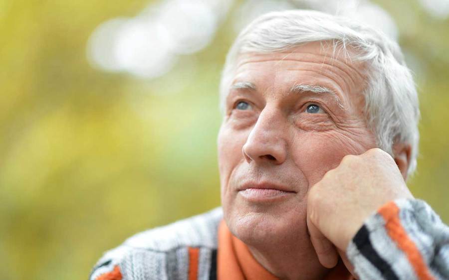 An elderly man looks away with a thoughtful look on his face in an outdoor setting.