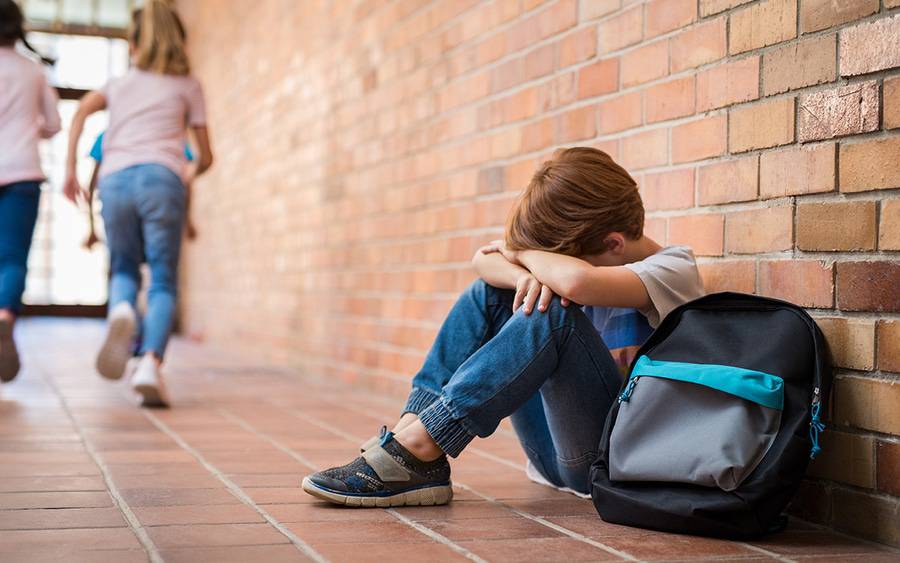 A boy sits with his head down at school after being bullied.