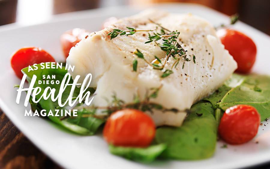 A plate of white fish with rosemary and cherry tomatoes on a bed of baby spinach represents a healthy diet that may help prevent cancer. As seen in San Diego Health Magazine.
