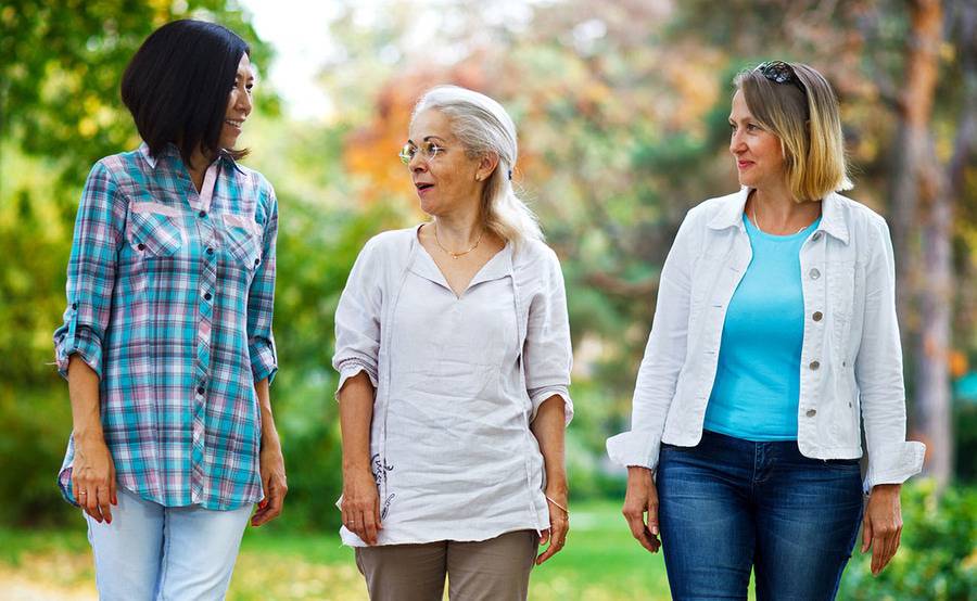 Three mature women walk in a park, representing the full life that can be led after treatment for gynecologic cancer.