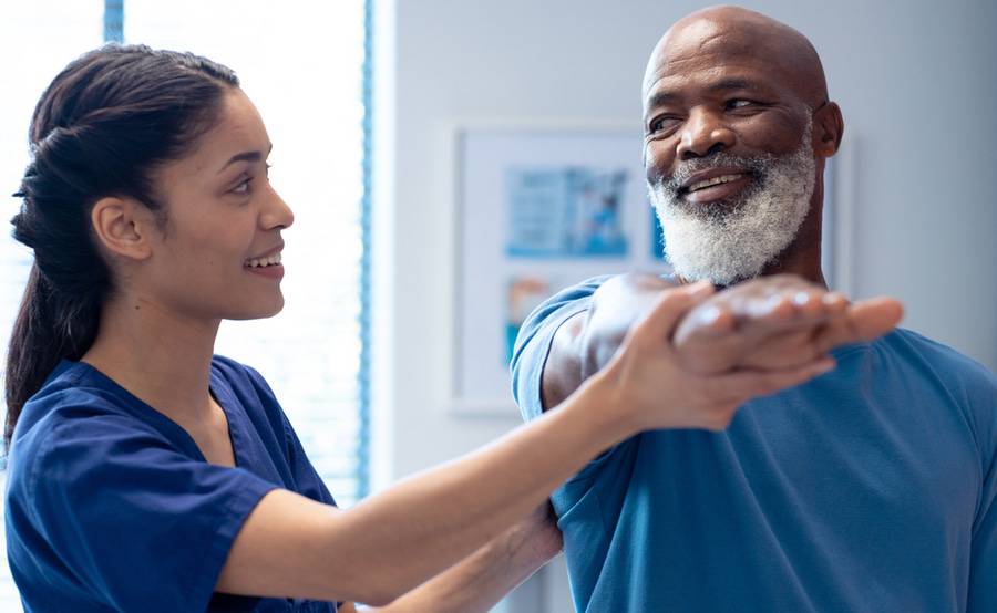 A physical therapist supports a patient's arm as he stretches to help with joint stiffness from cancer treatment.