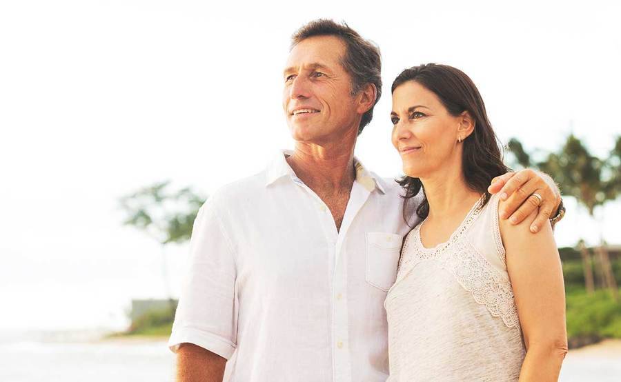 A smiling middle-aged Caucasian couple on the beach represents the confidence you can have in cancer screening at Scripps.