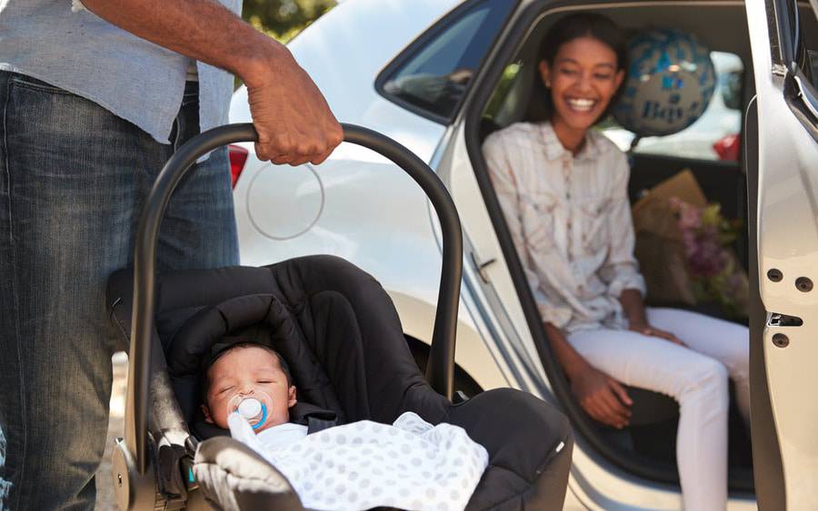 A young couple get ready to buckle their new baby into the backseat of their car.