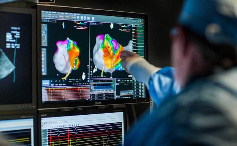 A physician in scrubs points to a digital screen showing a heart image in a darkened room.