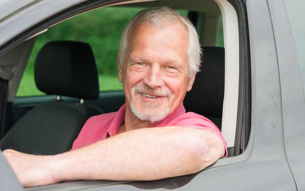 An older man with gray hair smiles as he sits inside his vehicle.