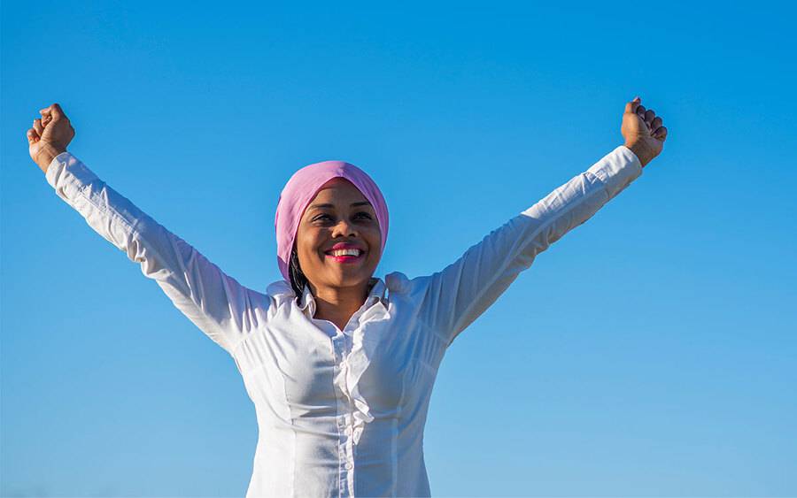 A black female cancer survivor wearing a white shirt and purple head scarf celebrates declining U.S. cancer death rates.