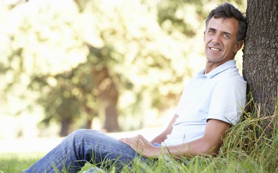 A man relaxes against a tree in an outdoor setting.