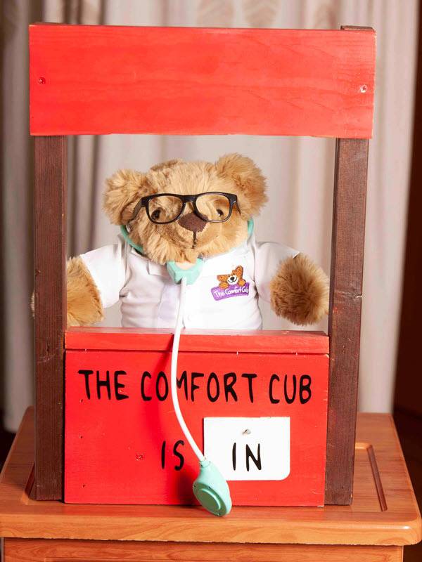 A Comfort Cub sits in a doctor's chair with a stethoscope. These teddy bears are designed to help adults ease the loss of a loved one.