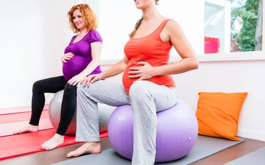 Two pregnant women sit on birthing balls and learn relaxation and breathing techniques in a prenatal class.