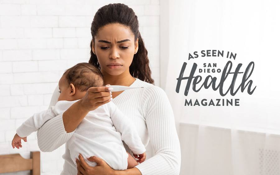 A young mom holds her baby while reading a thermometer.