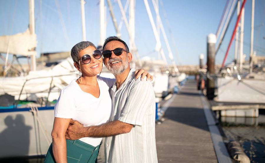 A middle-aged couple smiles at a boat dock.