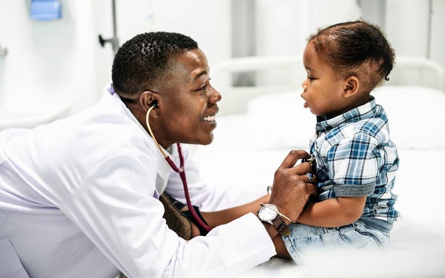 An African-American pediatrician smiles as he examines African-American child with stethescope.