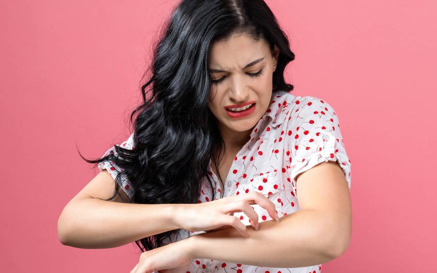 Young woman with psoriasis scratches her itchy arm.