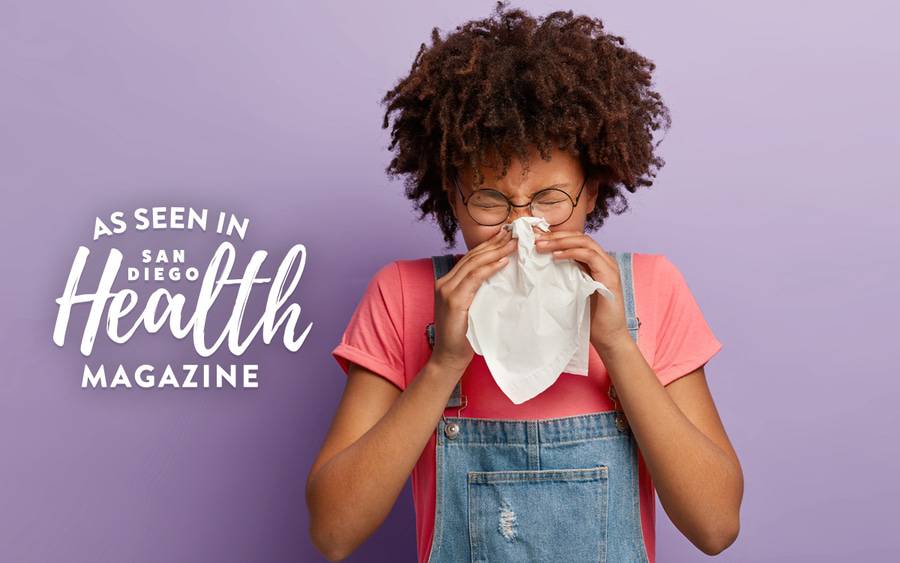 A woman in a bright color shirt sneezing into a tissue