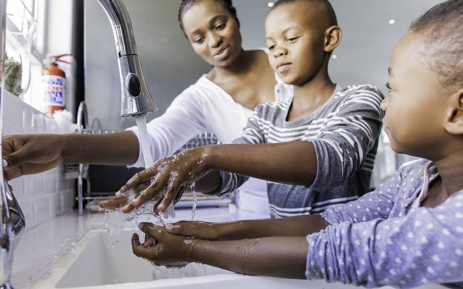 Mother watches son and daughter washing their hands to prevent COVID-19.