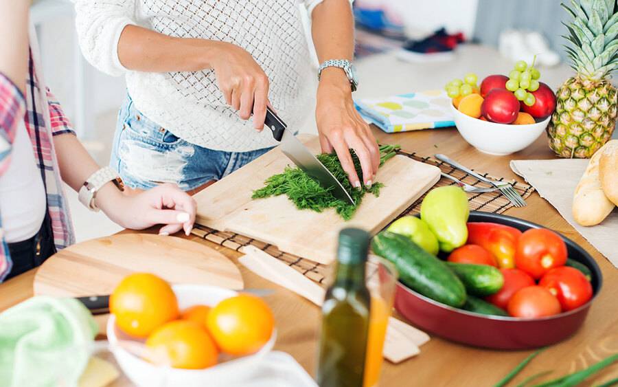 Two women cut herbs and vegetables, representing a cooking class.