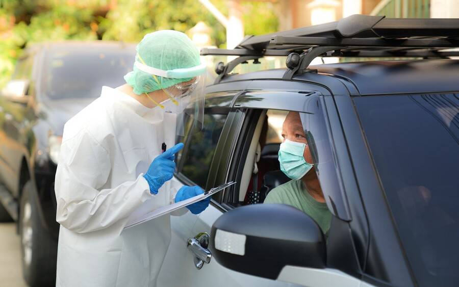An individual is wearing a mask in their car talking to a provider who will give them a COVID-19 PCR test.