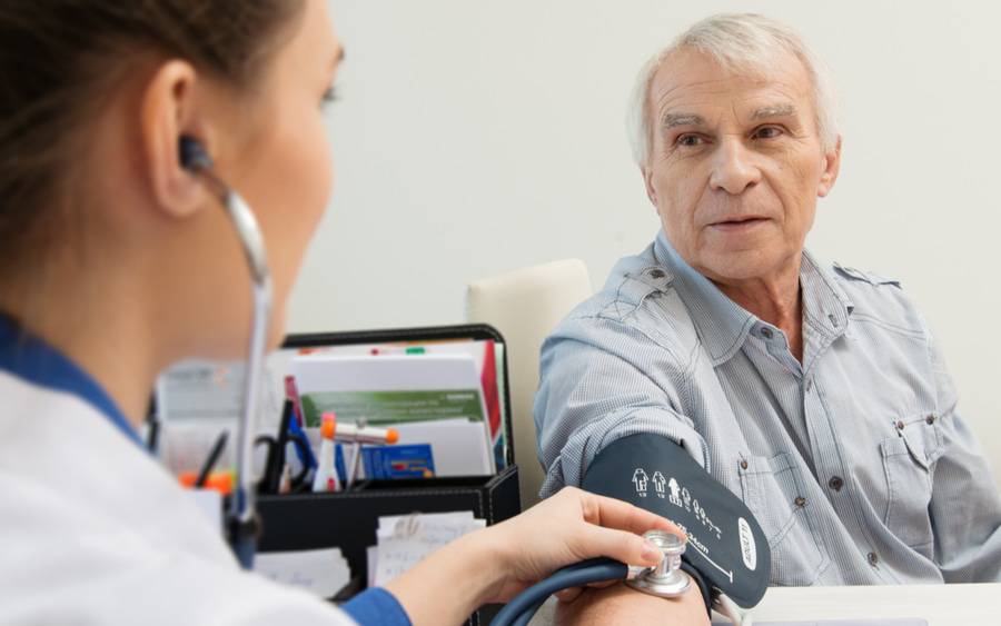 A nurse wearing a stethoscope checks the blood pressure of her senior patient.