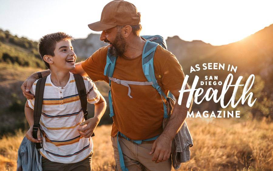 A father looking and smiling at his son who is smiling back while they are on a hike, demonstrating the benefits of the outdoors.