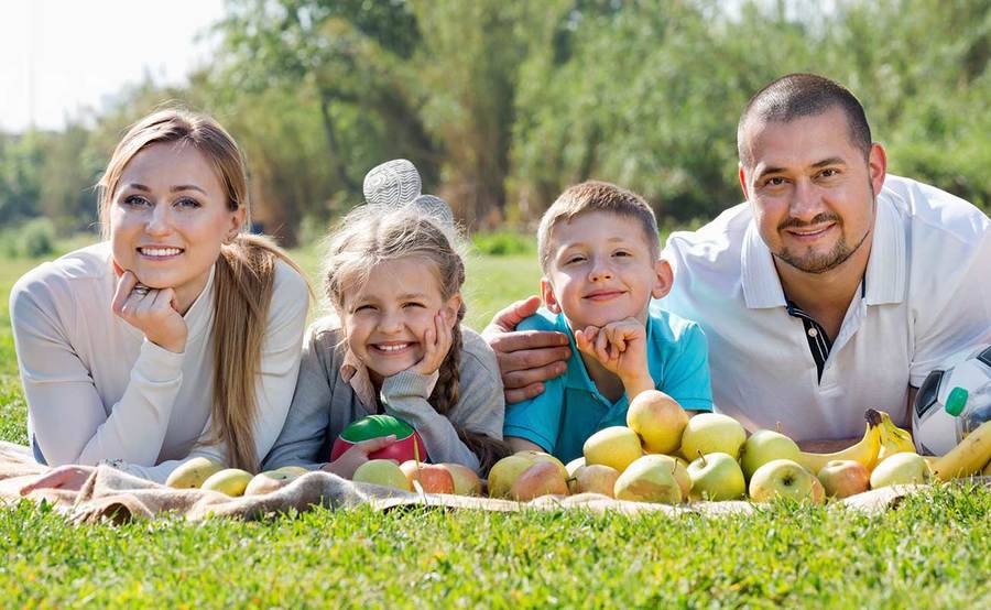 A smiling young family lays on a picnic blanket, representing a range of skin care and dermatology needs.