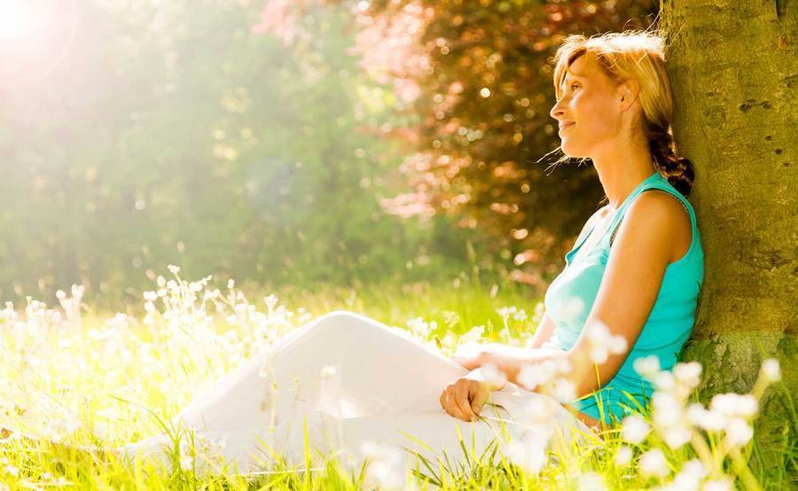 A smiling middle-aged woman under a tree represents the full life that can be led after desmoid tumor treatment.