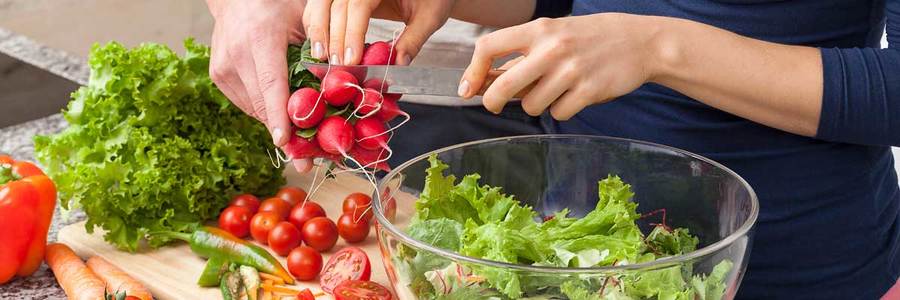 Close up photograph of two people preparing fresh produce for a salad in a kitchen setting.
