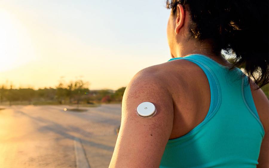 A woman is outdoors dressed for a run with a continuous glucose monitor visible on her upper arm.
