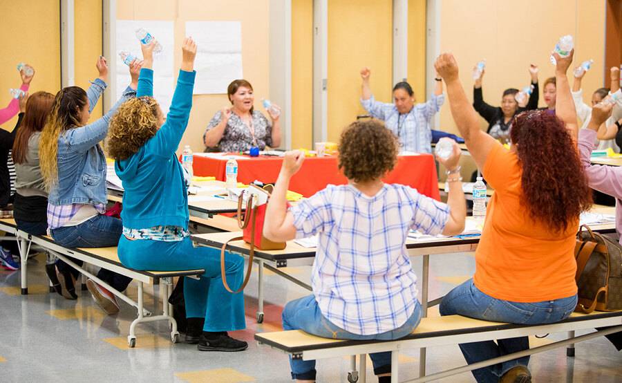 A female teacher leading a class as they raise both hands above thir head during an activity.
