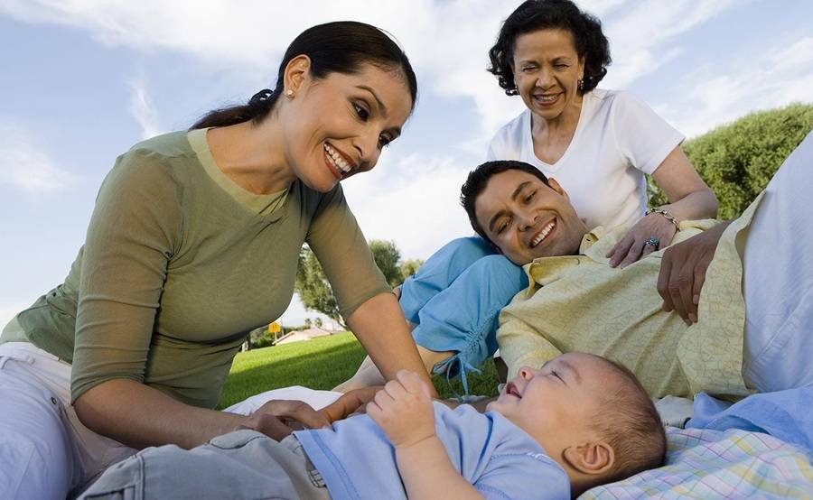A multigenerational family in a park smiles at their infant, representing a healthier life by preventing diabetes.