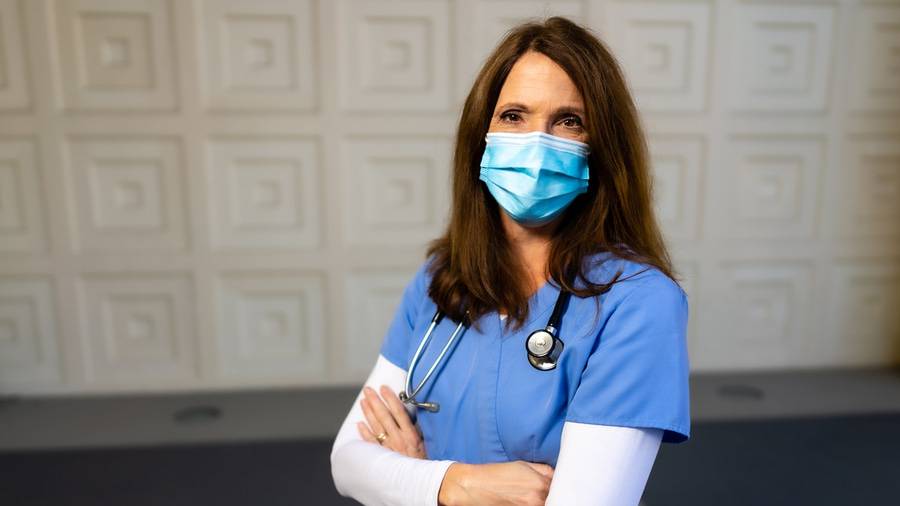 Dana Askew, RN standing outside in front of a white wall with a face mask on and stethoscope around her neck, one of the eight Scripps Nurses of the Year 2020.