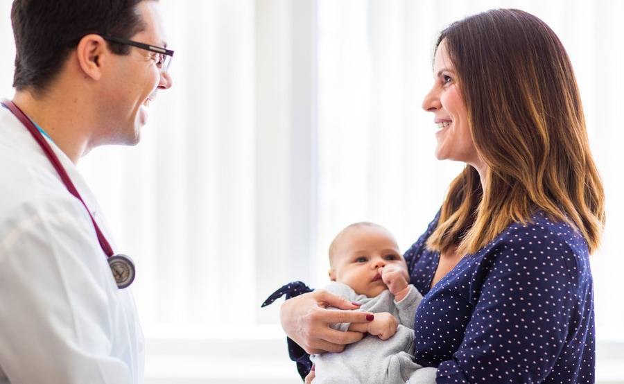 A young mom cradles her little baby as she interacts with a doctor during a visit.