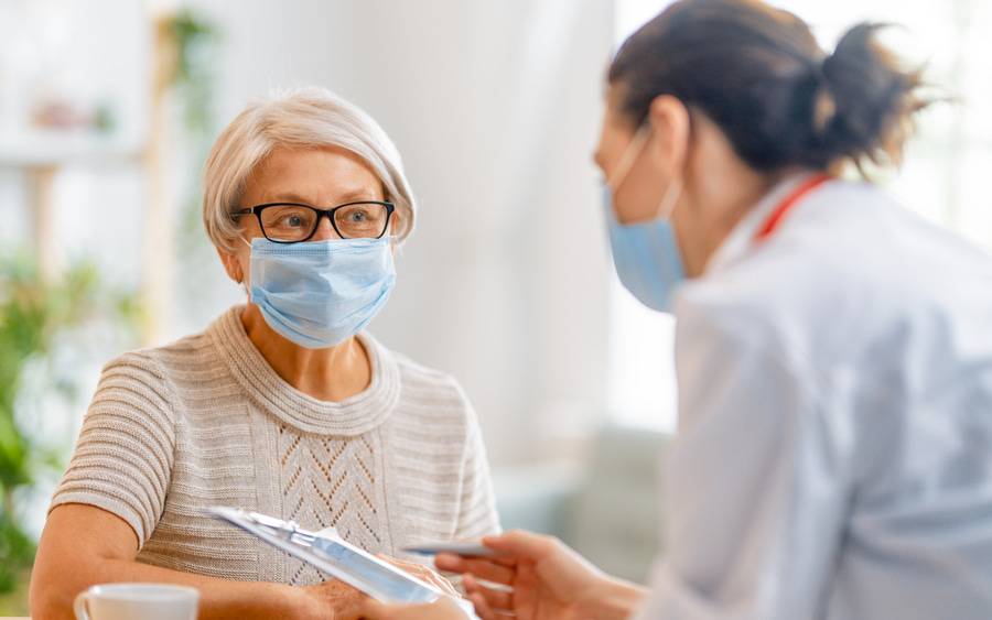 A mature woman has a discussion with her doctor, both wearing facemasks during the COVID pandemic.  