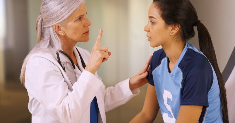 A doctor checks a girl soccer player for a head concussion.