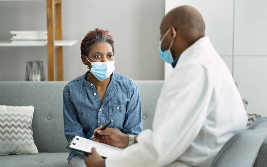 A patient wearing mask discusses her health with her doctor, also wearing a mask to protect against COVID.