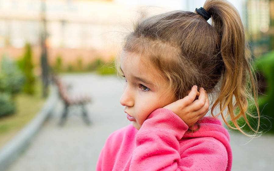A little girl grabs her ear, early sign of an ear infection.