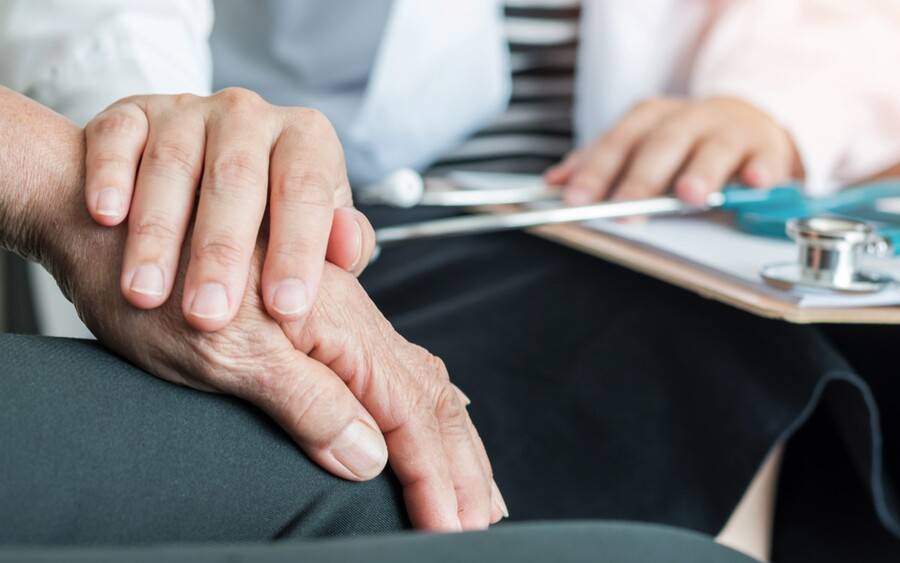 An elderly man with Parkinson's disease has his hand held by doctor.