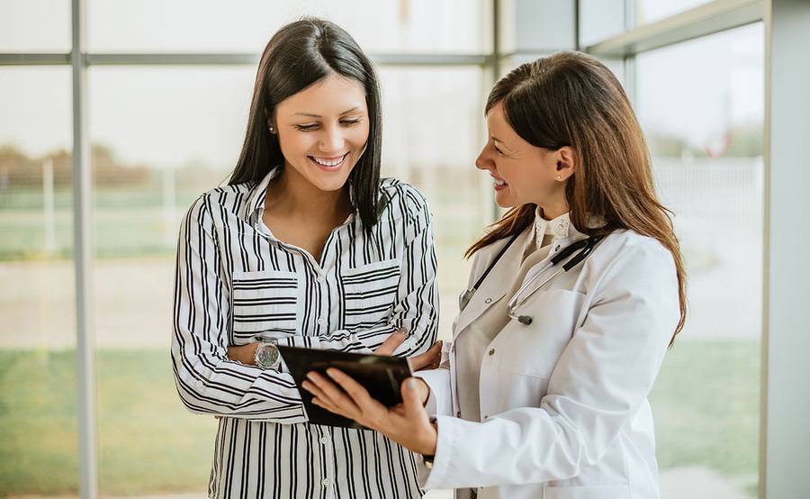 A woman smiling while talking with a physician who is also smiling.