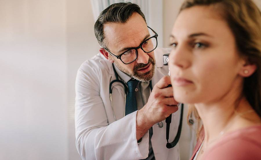 An Scripps ENT doctor thoroughly checks a female patient's ear with an otoscope.  