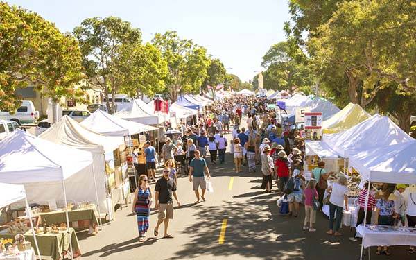 A crowd walks though a street fair of local vendors.