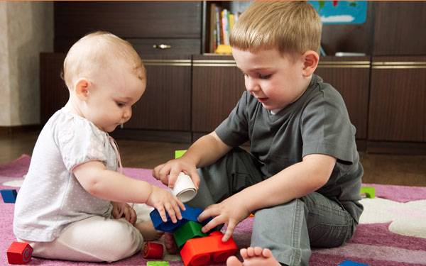 An infant and young boy play with blocks, representing the importance of introducing older kids to a new baby.